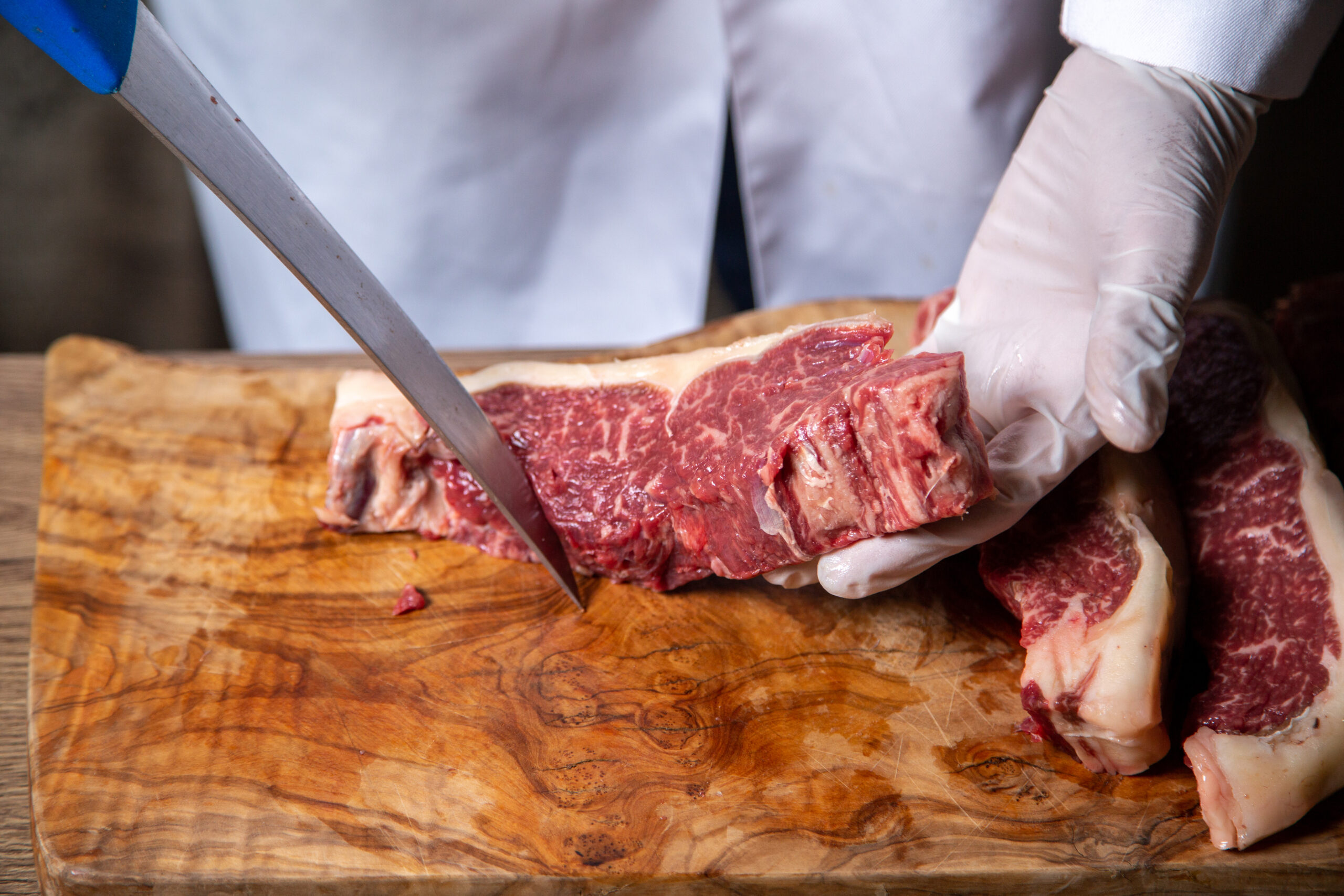 front view butcher cutting meat white gloves holding big knife wooden desk (1)